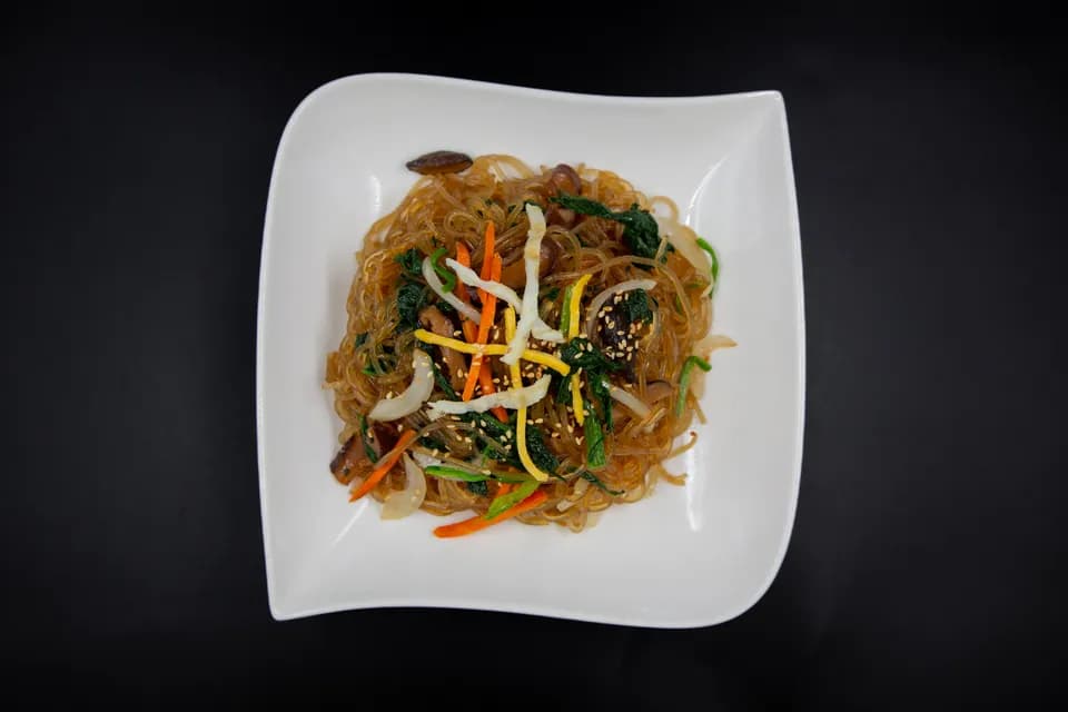 Japchae-Glasnudeln mit Gemüse und Sesam auf einem weissen Teller