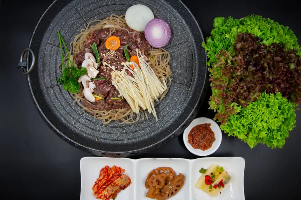 Mariniertes Rindfleisch mit Glasnudeln und Pilzen auf dem Tischgrill, dazu Salat und Banchan